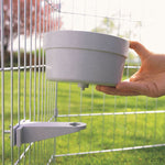 Load image into Gallery viewer, Hand holding a gray pet feeder against a wire cage with grass and trees in the background.