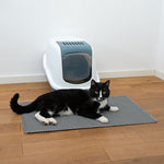 Load image into Gallery viewer, Cat lying on a mat next to a litter box in a room with wooden flooring.