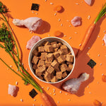 Load image into Gallery viewer, Bowl of brown cubes on an orange background with raw meat and vegetables
