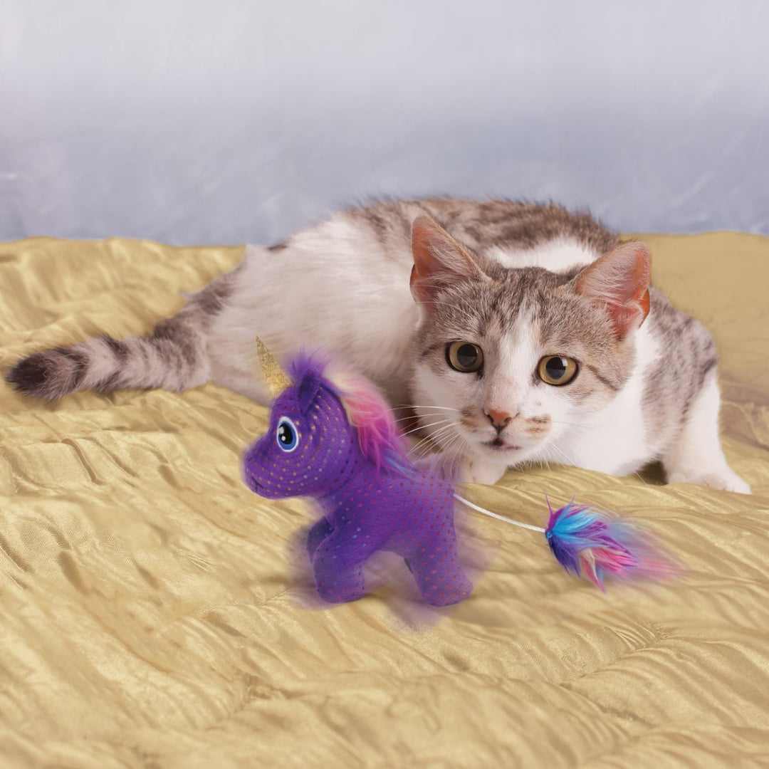 Cat playing with a purple unicorn toy on a bed