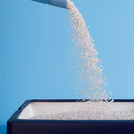 Load image into Gallery viewer, White granules being poured from a container against a blue sky
