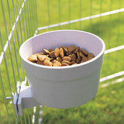 White bowl with pet food inside, attached to a cage with green grass background