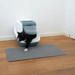 Load image into Gallery viewer, Cat using a litter box on a mat in a room with wooden flooring and white walls.

